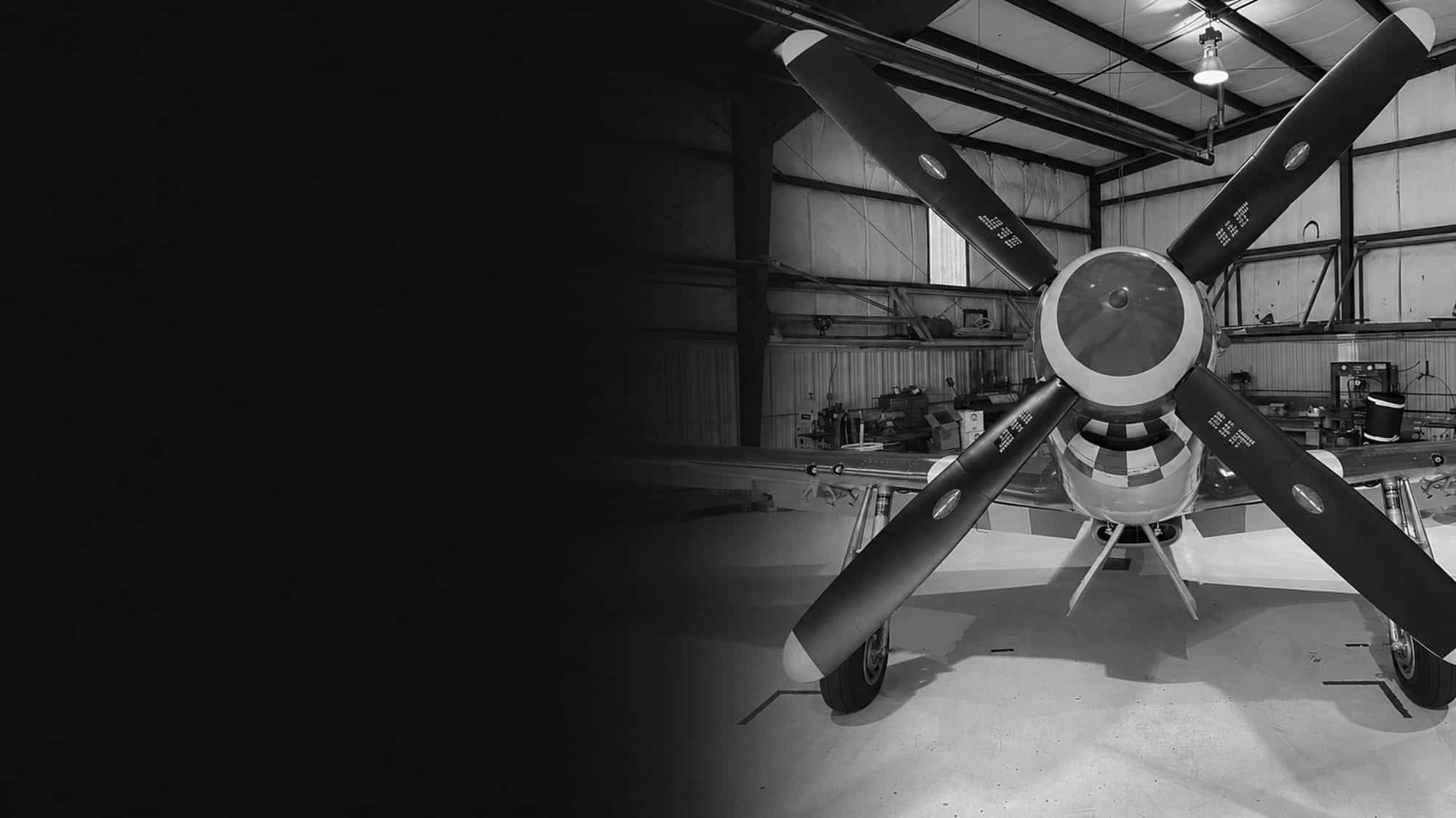 The propeller and polished spinner of an airplane parked in a darkened hangar.