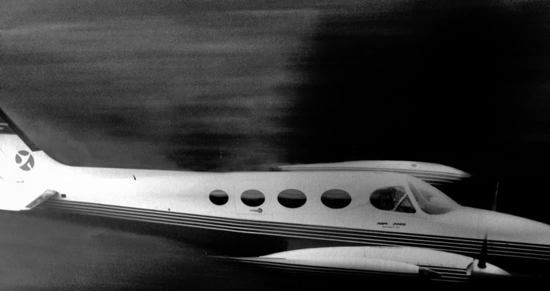 A twin engined Cessna 340 in flight above cloud, photographed in black and white.
