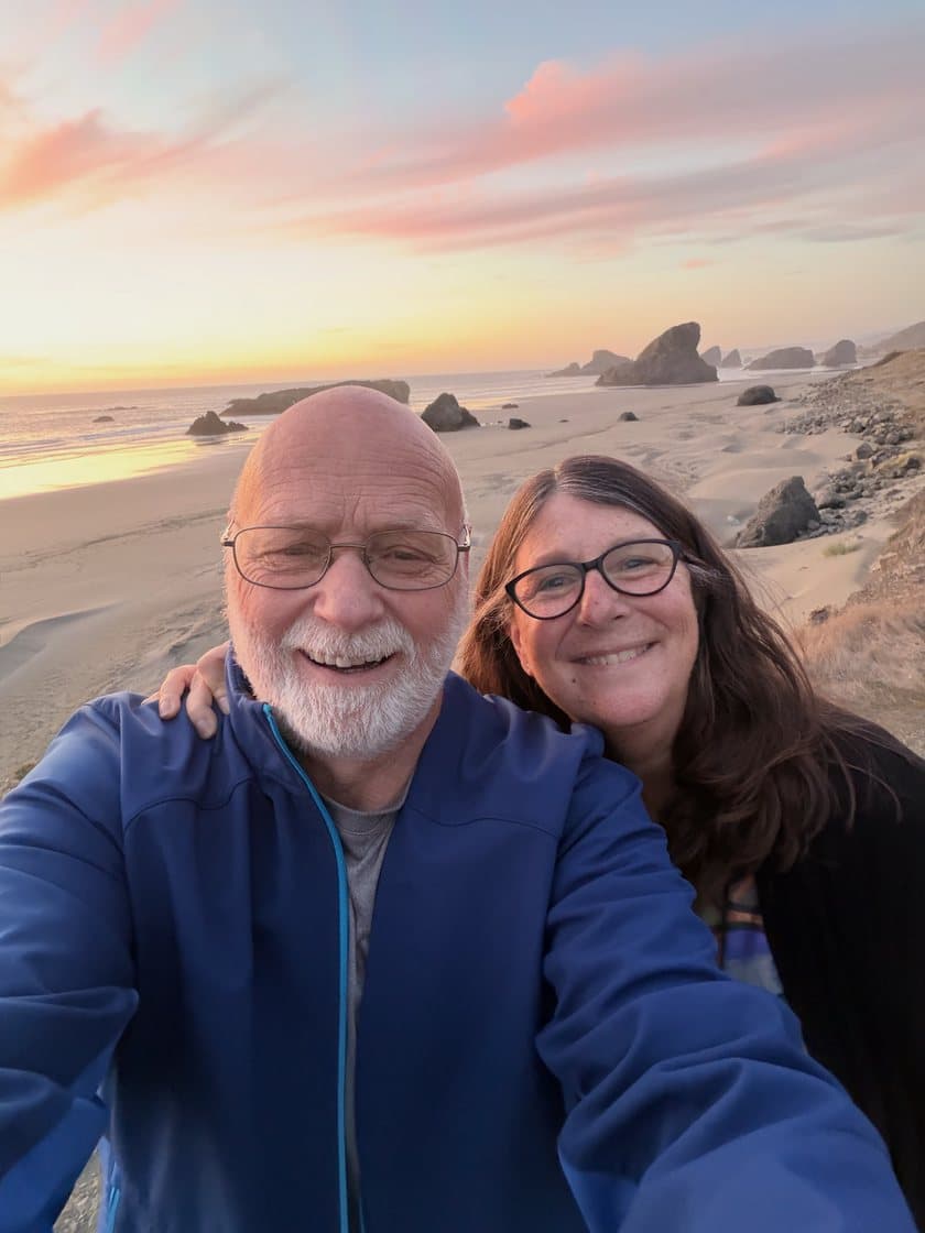 Jim Carpenter and his wife Cindy on a beach on the southern Oregon coast at sunset, sea stacks behind them.